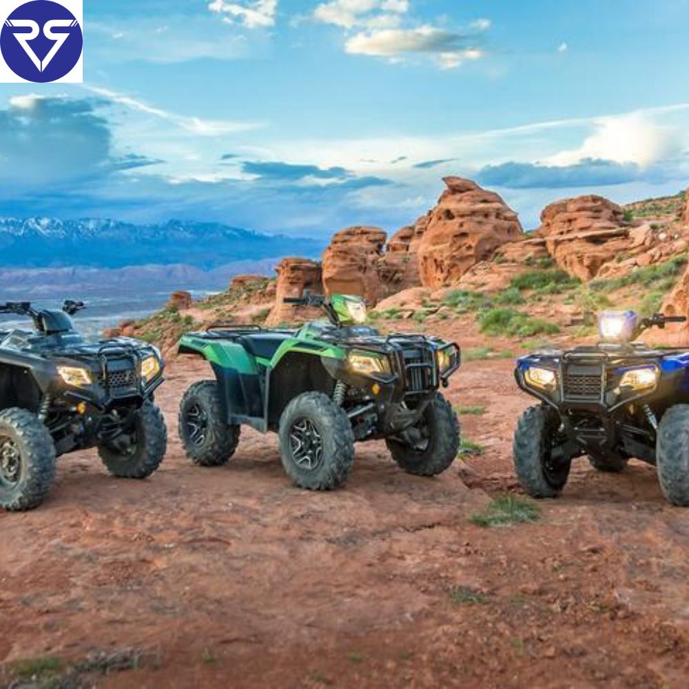 Three Honda ATVs parked on rocky desert landscape with red rock formations and mountains in background, showcasing off-road adventure under open sky.