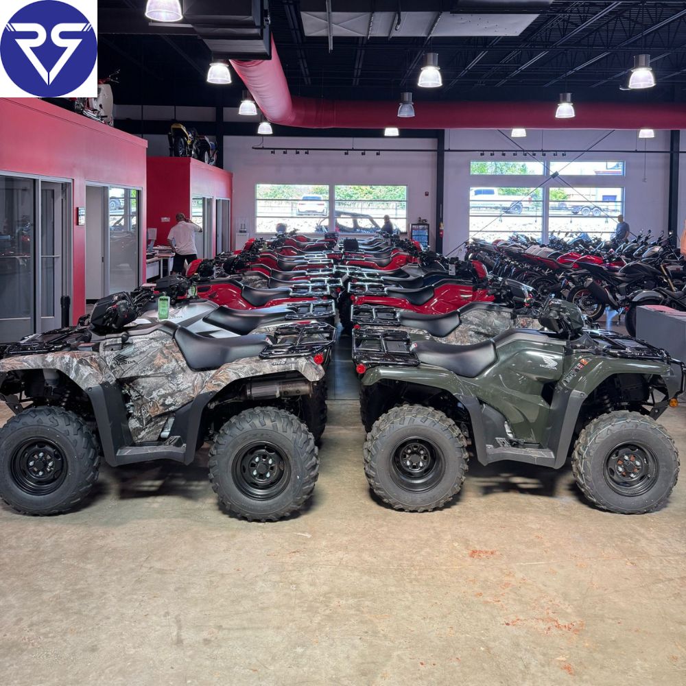 Indoor showroom with multiple Honda ATVs lined up, including camo and green models under bright overhead lighting
